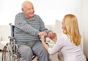 caregiver and elder man in a wheelchair holding hands