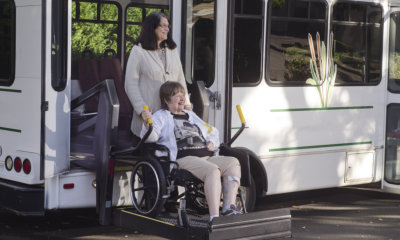 A woman in a wheelchair is helped off a van using a chair lift